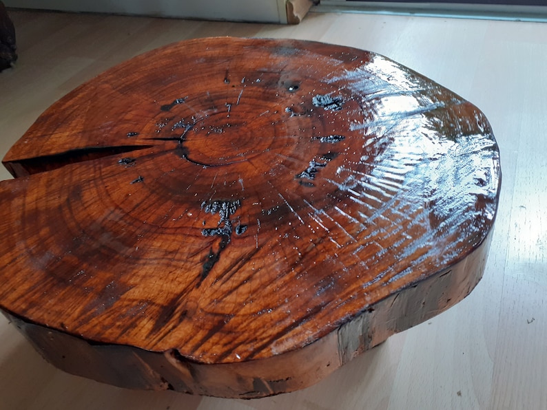 May include: A round, wooden table top with a natural, organic shape. The surface is a rich, dark brown with visible wood grain and a glossy finish. A large crack runs across the top. The table top is approximately 24 inches in diameter.
