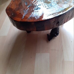 May include: A handcrafted, round coffee table made from a cross-section of a tree trunk. The tabletop is a rich, dark brown with a glossy finish, supported by three dark, carved legs. The table is approximately 30 inches in diameter.