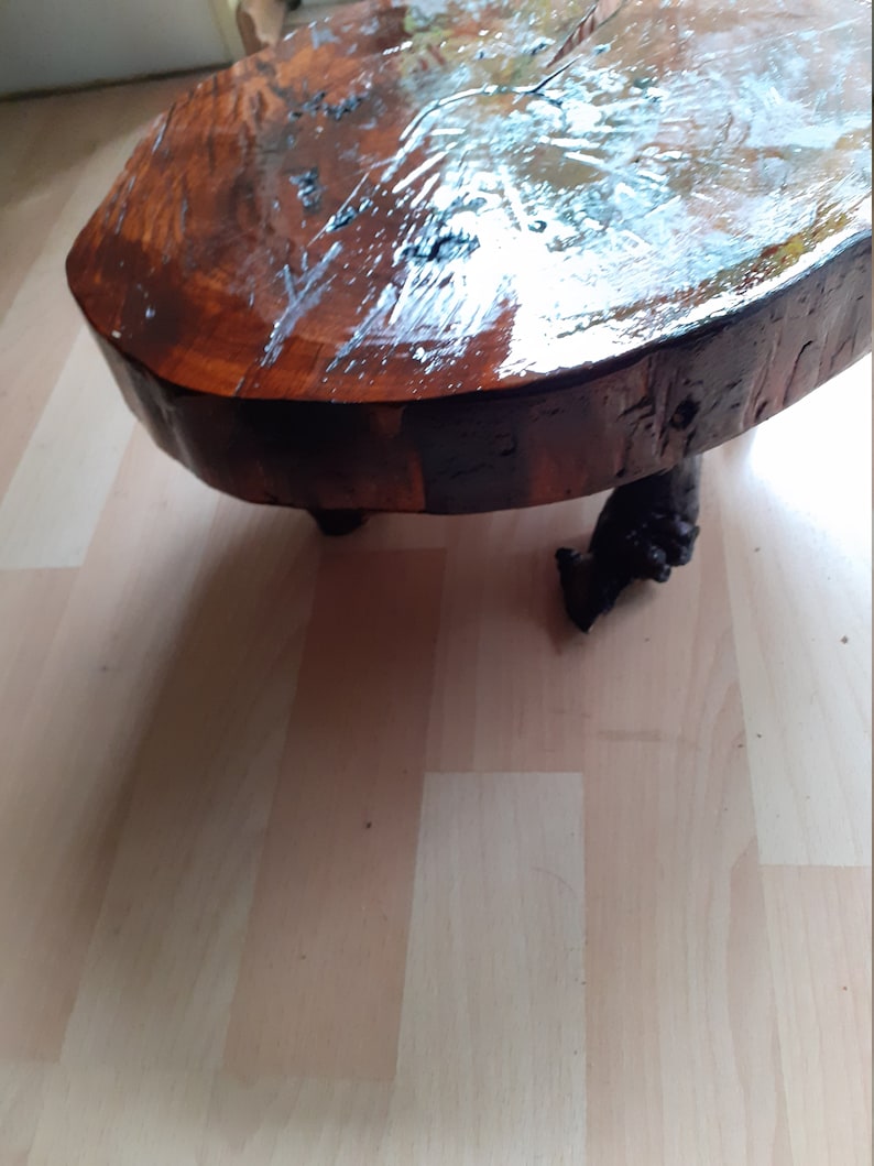 May include: A handcrafted, round coffee table made from a cross-section of a tree trunk. The tabletop is a rich, dark brown with a glossy finish, supported by three dark, carved legs. The table is approximately 30 inches in diameter.