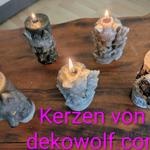 Könnte beinhalten: Fünf brennende Kerzen mit Wolfsmotiven. Die Kerzen sind in verschiedenen Grau- und Brauntönen gehalten, wobei die Flammen hell leuchten. Die Kerzen sind auf einer Holzoberfläche angeordnet.