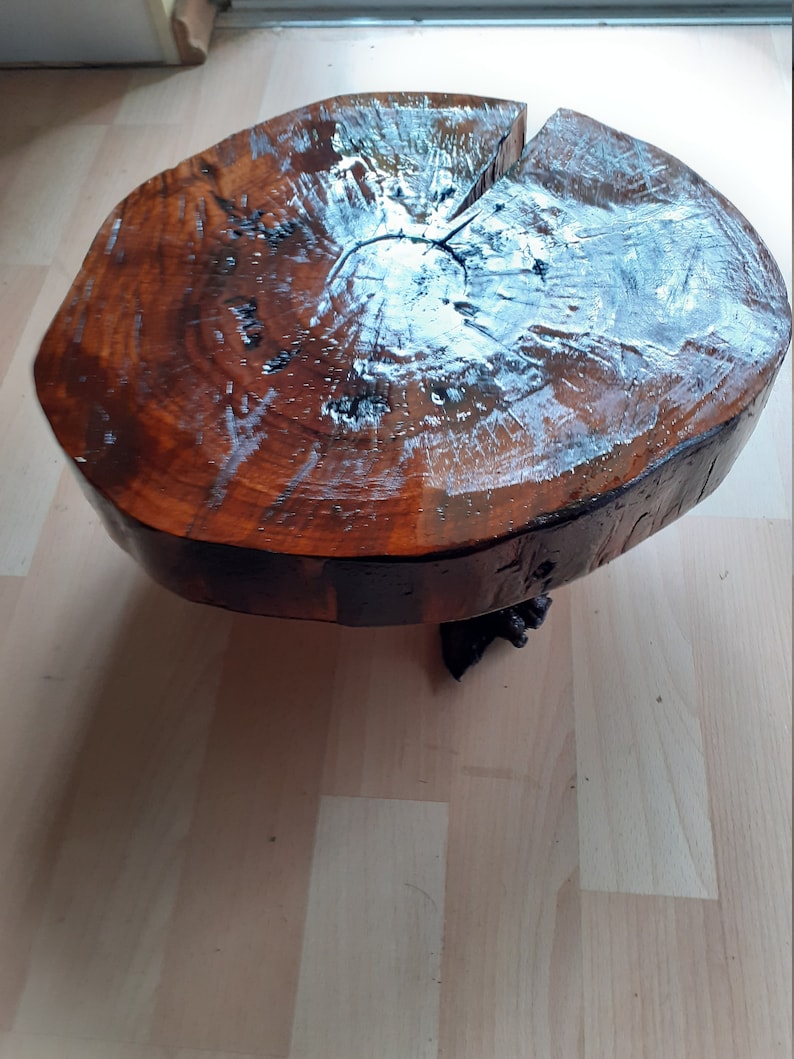 May include: A round, wooden side table with a natural, polished finish. The tabletop is a cross-section of a tree trunk, showcasing the wood's grain and color variations. The table is supported by a dark, decorative base.