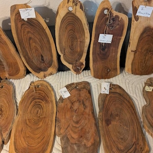 May include: A selection of ten wooden chopping boards, each with a distinctive shape and natural wood grain. They have a hole for hanging. Some boards have price tags attached. Measurements are in centimetres.