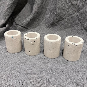 May include: Four small, white concrete planters with a speckled pattern. The planters are arranged in a row on a gray textured surface.