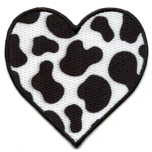 May include: Heart-shaped patch with a white background and black cow spots. The patch has a black border and is made of a textured fabric. The design is a playful take on a classic pattern.