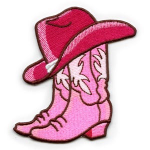 Op de afbeelding: Geborduurde patch met een roze cowboyhoed en -laarzen. De hoed is donkerroze met een bruine rand en de laarzen zijn lichtroze met een decoratief ontwerp. De patch is bedoeld om op stof te strijken of te naaien.