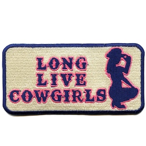 Può includere: Toppa ricamata con la scritta "LONG LIVE COWGIRLS" in rosa e blu navy. La toppa presenta una silhouette di una cowgirl in blu navy su sfondo beige, con un bordo blu navy.