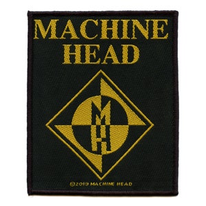 Könnte beinhalten: Ein schwarzer und goldener gestickter Aufnäher mit dem Text "MACHINE HEAD" und einem Logo mit einem stilisierten "MH" in einem Diamanten.