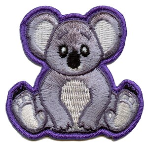 May include: Purple embroidered koala bear patch with white accents. The koala is sitting with its arms crossed and has a cute expression on its face.
