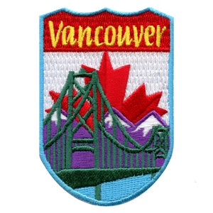 May include: An embroidered patch with a red, white, and blue shield shape. The top of the shield has the word "Vancouver" in yellow letters. The center of the shield has a green bridge with a red maple leaf behind it. The bridge is over purple mountains with white snow peaks.