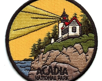 Könnte beinhalten: Ein runder gestickter Aufnäher mit einem Leuchtturm auf einer felsigen Klippe, von dem ein Lichtstrahl ausgeht. Der Text "Acadia National Park" ist in braunen Buchstaben am unteren Rand des Aufnähers angebracht.