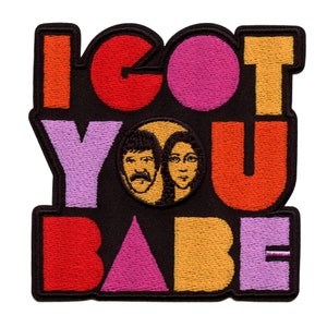 Può includere: Toppa ricamata con il testo "I GOT YOU BABE" in lettere colorate. Le lettere sono contornate di nero e hanno uno stile retrò. Un cerchio con due facce all'interno si trova al centro della toppa.