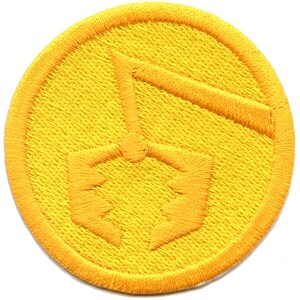May include: Yellow embroidered patch with a stylized design of a hand holding a weapon. The patch is circular and has a yellow border.