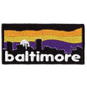 May include: Embroidered patch with a black silhouette of the Baltimore skyline against a purple and yellow sunset. The word "baltimore" is written in white below the skyline.