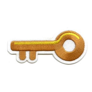 May include: A gold-colored key with a yellow outline, embroidered on a white fabric patch.