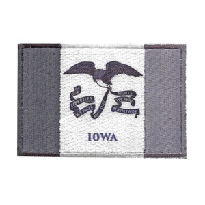 May include: A grey and white embroidered patch featuring the state flag of Iowa. The flag depicts a blue eagle with a red beak and talons, and a scroll with the words "Our Liberties We Prize and Our Rights We Will Maintain". The word "Iowa" is printed in blue below the eagle.