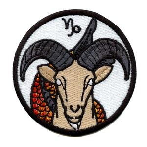 Op de afbeelding: Gestikte patch met een zwart en bruin geitenhoofd met een rood en oranje visstaartontwerp. De patch is rond en heeft een witte achtergrond met een zwarte rand. De tekst "♑" is zichtbaar in het midden bovenaan de patch.