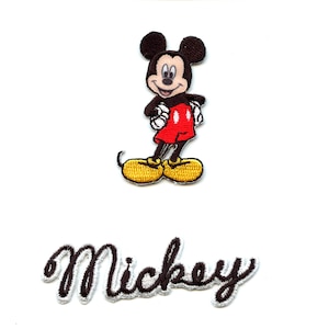 Puede incluir: Parche bordado para planchar con Mickey Mouse en su característico pantalón rojo y zapatos amarillos. El parche también incluye la palabra "Mickey" en una fuente cursiva.