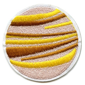 May include: A round, embroidered patch depicting Jupiter, the largest planet in our solar system. The patch features a white background with brown and yellow stripes, representing the planet's iconic cloud bands.