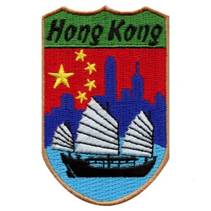 May include: Embroidered patch with a shield shape, featuring a green background with the text "Hong Kong" in black. The shield also features a red background with a yellow five-pointed star and four smaller stars, a blue skyline, and a white sailboat with black sails.