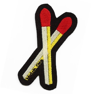 May include: Two red and yellow matchsticks crossed over each other, embroidered on a black fabric patch.