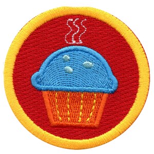 Könnte beinhalten: Ein runder, roter gestickter Aufnäher mit gelbem Rand. Der Aufnäher zeigt einen blauen Cupcake mit orangefarbenem Frosting und weißen Streuseln. Aus dem Cupcake steigt Dampf auf.