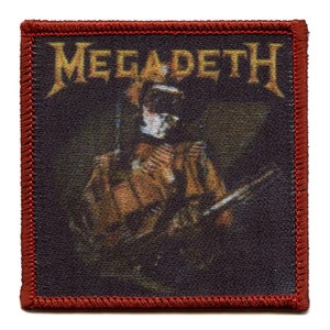 May include: A red embroidered patch with the band name "Megadeth" in gold lettering. The patch features a dark image of a person wearing a gas mask and holding a weapon.