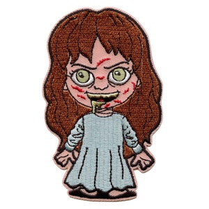 May include: Embroidered patch of a cartoon girl with brown hair, wearing a blue dress and has red and green markings on her face.