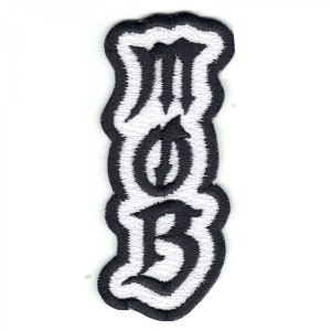 May include: Embroidered patch in black and white. The patch features the letters "MOB" in a gothic font. The letters are black with a white border. The patch has a wavy, irregular shape.