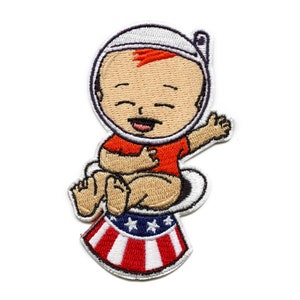 May include: Embroidered patch of a cartoon baby astronaut wearing a red shirt and a white helmet, sitting on a toilet with an American flag design.