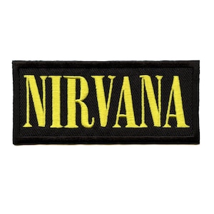 May include: Black rectangular patch with the word "NIRVANA" embroidered in yellow. The patch has a black border and is likely made of fabric. The yellow text is in a bold, sans-serif font.
