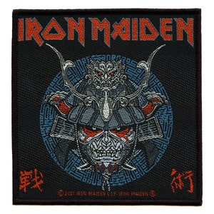 Op de afbeelding: Vierkante zwarte patch met de bandnaam "IRON MAIDEN" in oranje. De patch heeft een gedetailleerde illustratie van een samoerai-krijger met een schedelgezicht, rode accenten en een blauwe cirkelvormige achtergrond. De teksten "戦" en "術" zijn ook zichtbaar.
