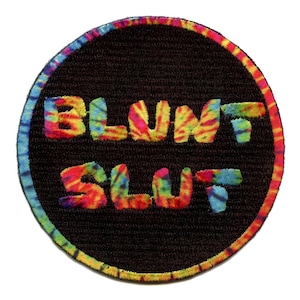 May include: A round, tie-dye patch with the words "BLUNT SLUT" in a rainbow color scheme.