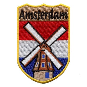 Pode incluir: Um remendo bordado com um moinho de vento e a bandeira holandesa, com a palavra "Amsterdam" acima. O remendo tem a forma de um escudo e uma borda amarela.