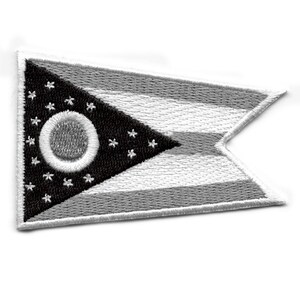 May include: A black and white embroidered patch of the Ohio state flag. The flag features a white circle with a smaller gray circle inside, surrounded by 17 white stars on a black triangular background. The flag is bordered by white stripes.