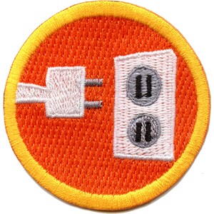 May include: A round orange patch with a yellow border. The patch features a white electrical outlet with two gray plugs and a white electrical cord with a gray plug.