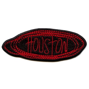 May include: Black and red embroidered patch with the word "HOUSTON" in red script. The patch has a black oval shape with red stitching around the edges and the word "HOUSTON" in the center.