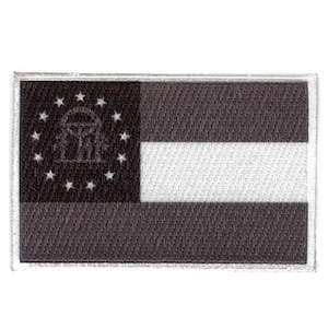 May include: Black and white embroidered patch featuring the state flag of Georgia. The flag has a white stripe across the center and a black field with a gold star-shaped circle containing the state seal. The seal depicts a gold archway with three pillars and a gold dome.