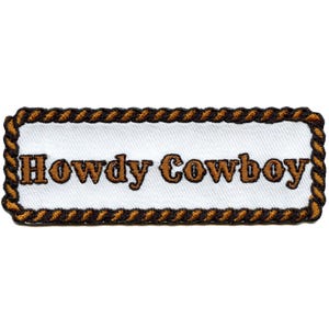 Può includere: Una toppa rettangolare con le parole "Howdy Cowboy" ricamate in marrone su sfondo bianco. La toppa è bordata da un disegno a corda marrone e beige.