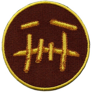 May include: A brown embroidered patch with a yellow outline. The patch features a stylized face with a frown and a set of teeth.