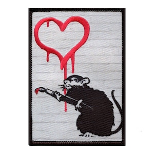May include: A black and white embroidered patch of a rat holding a paintbrush and painting a red heart on a white background.