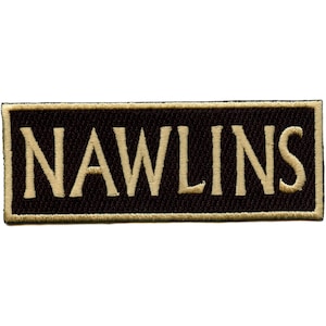 May include: Embroidered patch with the word "NAWLINS" in gold thread on a black rectangular background. The patch has a gold border. The letters are in a bold, sans-serif font.
