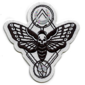 May include: Black and white embroidered patch of a moth with a skull head, surrounded by geometric shapes and a crescent moon with iridescent thread.