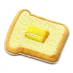 May include: An embroidered patch depicting a slice of bread with a pat of butter on top.