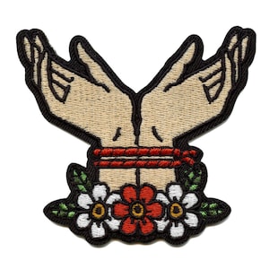 May include: Embroidered patch featuring two hands tied together with red rope and surrounded by green leaves and white and red flowers.