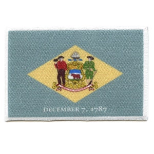 May include: A blue and yellow embroidered patch featuring the state seal of Delaware. The seal depicts a farmer and a soldier standing on either side of a shield with a plow and an ox. The text "DECEMBER 7, 1787" is printed below the seal.