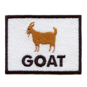 Op de afbeelding: Een witte geborduurde patch met een bruine geit en het woord "GOAT" in zwarte letters.