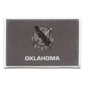 May include: A grey embroidered patch featuring the state seal of Oklahoma. The seal depicts a stylised Native American headdress with a feather and the word "OKLAHOMA" below.