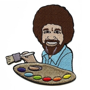 May include: Embroidered patch featuring a smiling man with a brown afro, beard, and blue shirt, holding a paintbrush and a color palette with various paint colors. The patch is designed with detailed stitching and a white background.