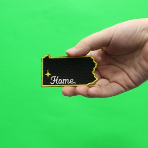 May include: A black felt patch in the shape of the state of Pennsylvania with yellow stitching around the border. The patch has a white star and the word "Home" embroidered in white.