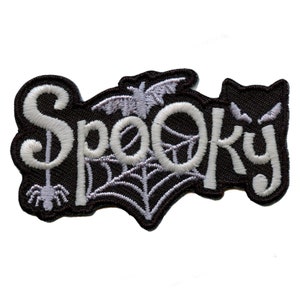 Pode incluir: Etiqueta de ferro bordada preta com letras brancas que diz "Spooky" com um design de aranha, morcego e teia de aranha.